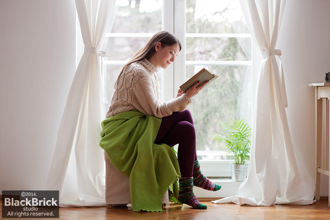 Photo of young woman reading a book by the window