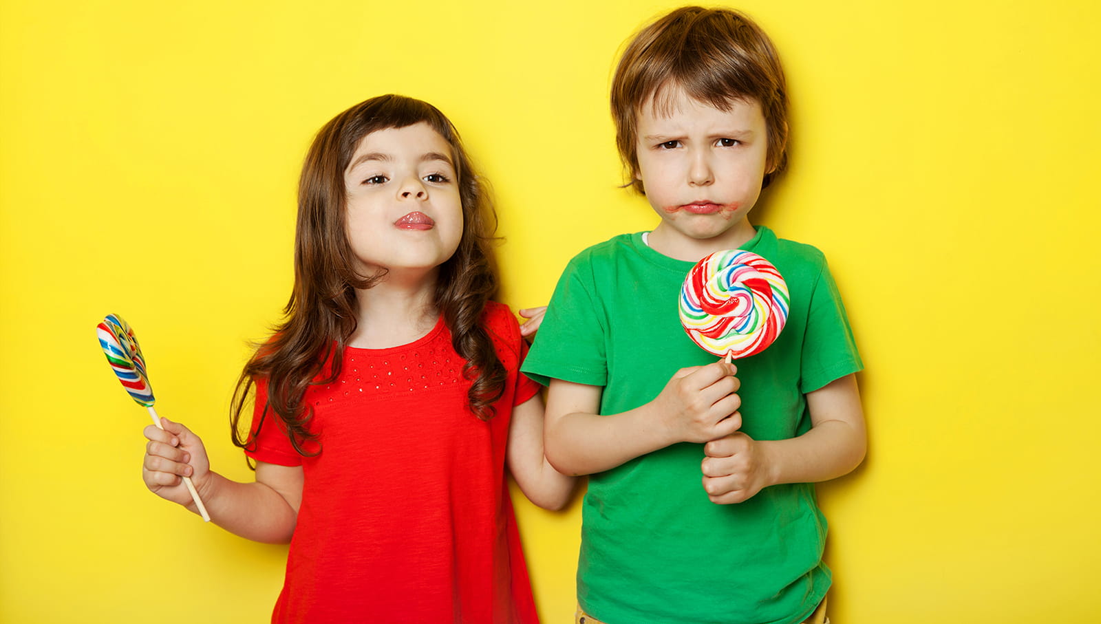 Studio portrait of cute children with lollipops on yellow background